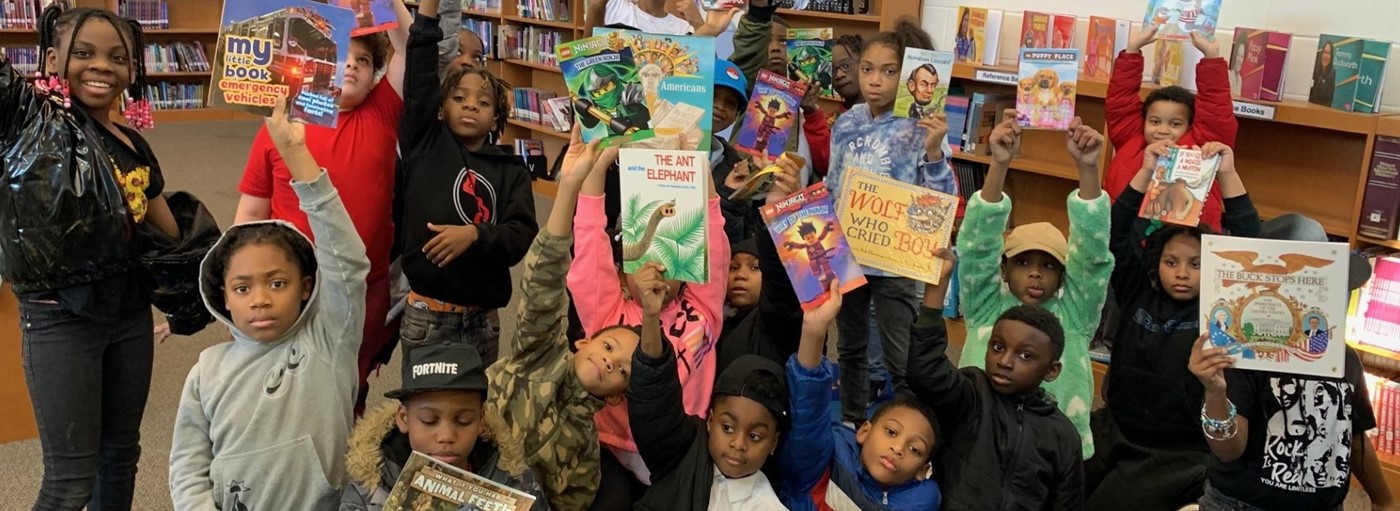 Students hold up books received during the Read Across America Book Gifting Event